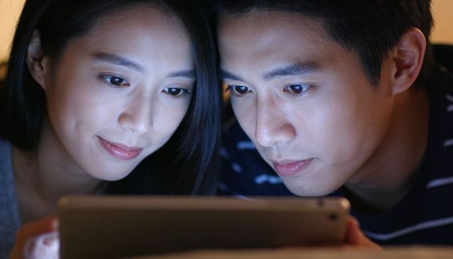 Couple leaning close sharing tablet under blue screen glow late night home intimacy