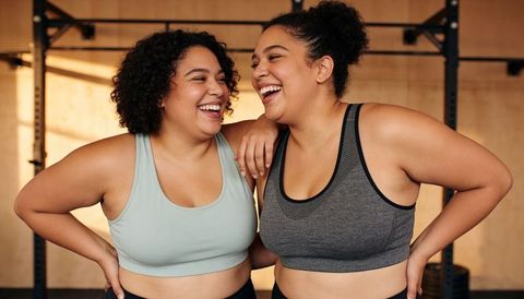 Two women laughing after workout in gym sports bras celebrating friendship and fitness