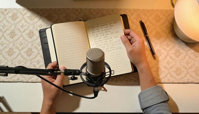 Creator recording podcast reading notes at cozy home workspace with condenser microphone