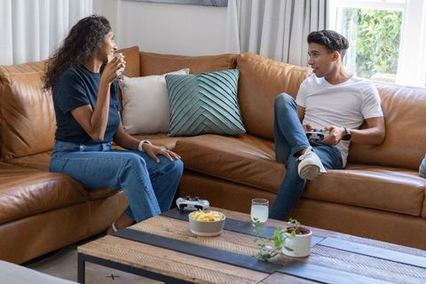 African american couple lounging on leather sofa sharing drink and playing video game