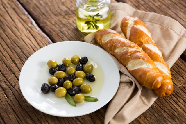 This image showcases a plate of marinated olives drizzled with olive oil, accompanied by fresh bread on a rustic wooden table. Ideal for use in food blogs, Mediterranean cuisine promotions, healthy eating articles, and restaurant menus.