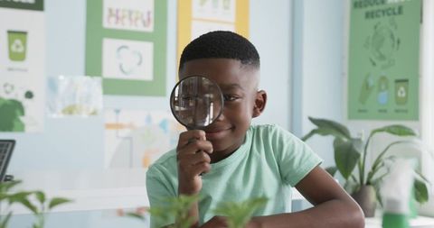 Young african boy examining classroom plant with magnifying glass for science learning