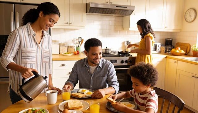 Sunlit family breakfast pouring coffee at kitchen table, parents and kids sharing meal