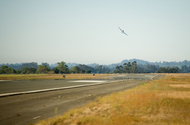 A small aircraft is taking off from the runway at Charles M. Schulz Sonoma County Airport during the 2011 Green Flight Challenge. Sponsored by Google, this event was organized by NASA and the Comparative Aircraft Flight Efficiency (CAFE) Foundation to promote advancements in fuel efficiency and reduced emissions using renewable fuels and electric aircraft. The image depicts the rising aircraft against a backdrop of grassy fields and distant trees detailing the outskirts of the airport. This image is ideal for illustrating articles on aviation innovation, sustainable aviation technology, or events hosted by NASA and related foundations.