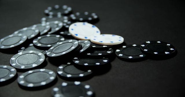 Poker chips with black and white colors scattered on a black table. Suitable for content related to casinos, gambling, betting, entertainment, and game night themes.