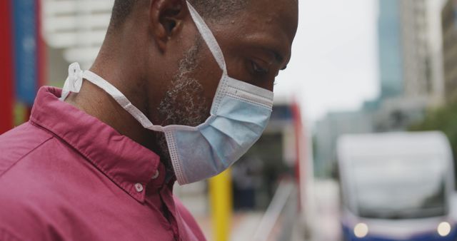African American man out and about in the city streets during the day, wearing a face mask against air pollution and covid19 coronavirus, using his smartphone while crossing the street.