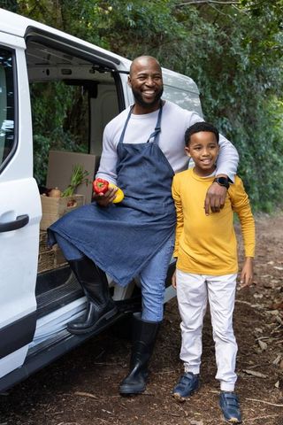 African american farmer and son delivering fresh produce, smiling by white van