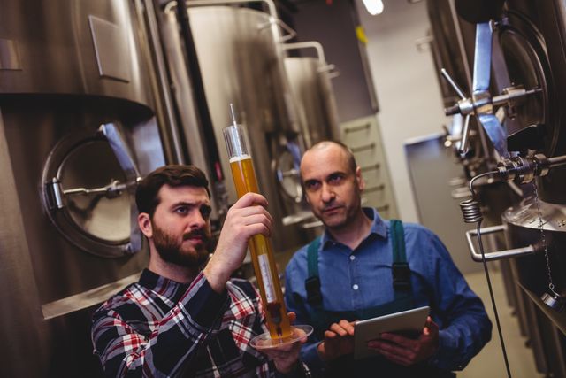 Manufacturer inspecting beer in tube with worker at brewery