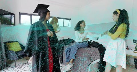 Graduate in cap and gown celebrating with friends in dorm room before ceremony