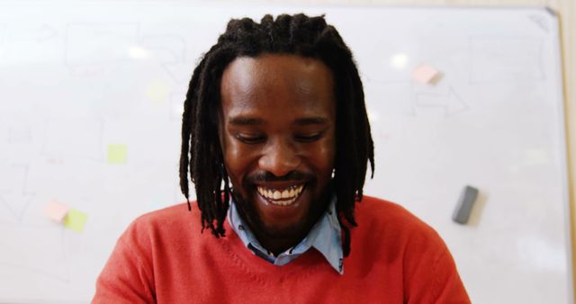 A cheerful African American man with dreadlocks is smiling, with copy space available above his head. His joyful expression suggests a positive and relaxed atmosphere, in a casual work or educational setting.