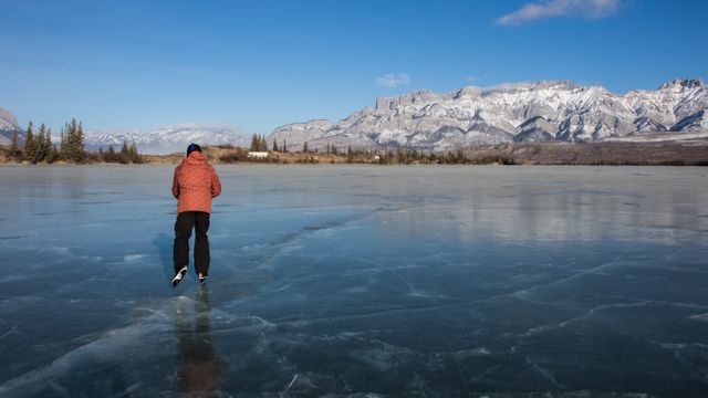 Person enjoying ice skating on a frozen lake surrounded by stunning snow-capped mountains. Winter activity emphasizes serene and picturesque scenery, perfect for travel brochures, winter sports promotions, and nature-themed websites.