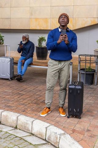Young traveler checking eta on smartphone while waiting with suitcase at urban plaza