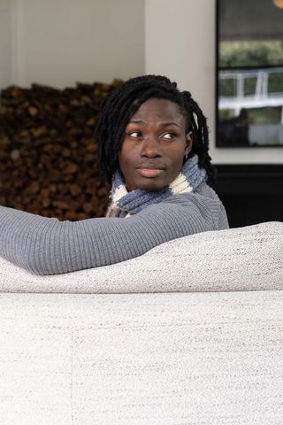 African american woman relaxing on sofa wearing knit scarf near stacked firewood