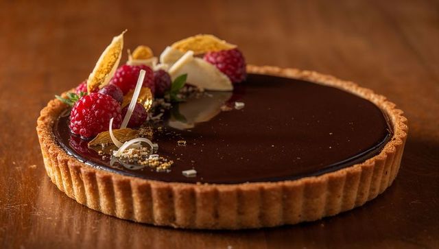 Glossy chocolate ganache tart with raspberries and gold leaf on rustic wood
