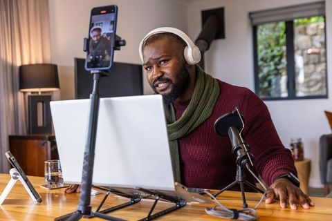 African american man streaming podcast and recording video in home studio with laptop mic