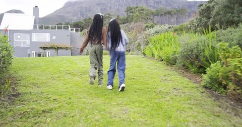 African American Teen Girls Walking Up Garden Slope Toward Modern Suburban House