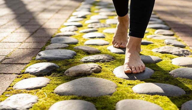 Barefoot walking on mossy stone path with sunlit rays and textured brick pavers