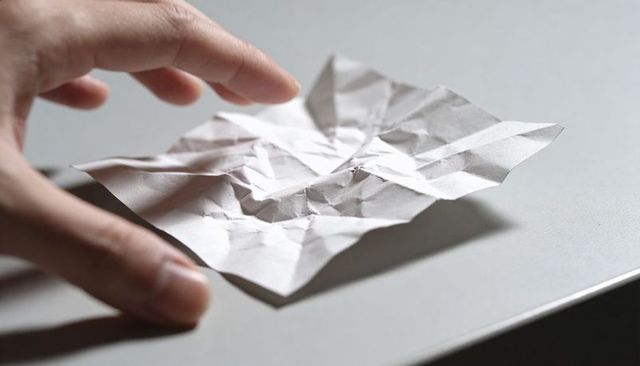 Hand reaching toward crumpled paper on minimal gray desk conveying frustration