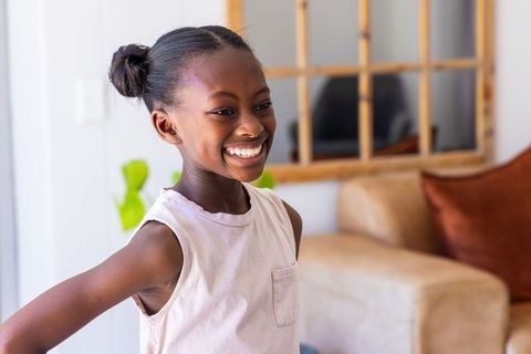 African girl smiling and standing in bright living room wearing sleeveless top