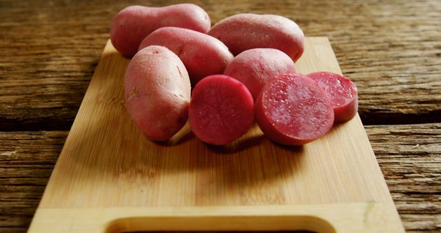 Sliced red potatoes rest on a wooden cutting board, showcasing their vibrant interior. Potatoes like these are a staple in many cuisines and valued for their versatility in cooking.