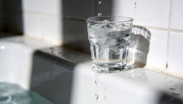 Iced glass dripping on white tile ledge under bright sunlight with crisp water reflections