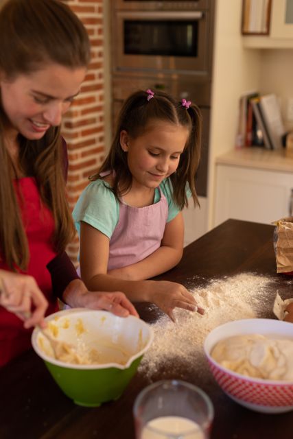 Side view of a caucasian girl leaning on the kitchen desk baking with her mother beside her. she's preparing the flour while her mother mixes ingredients in a bowl.