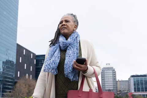 Senior african american woman walking in city plaza holding smartphone and red tote