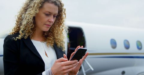 Confident Businesswoman Using Smartphone Beside Private Jet