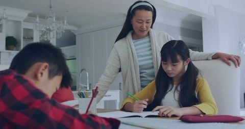 Mother guiding daughter through homework at bright kitchen table, focused family study