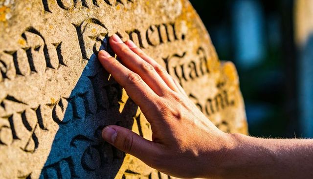 Tracing gothic gravestone lettering with hand casting shadow in sunlit cemetery