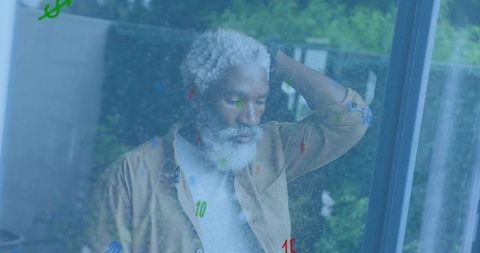 Contemplative senior man standing by window scratching head with colorful digit reflections