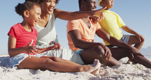 Smiling african american family sitting and embracing on sunny beach. healthy, active family beach holiday.