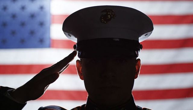 Silhouetted us marine saluting in front of american flag backdrop for patriotic tribute