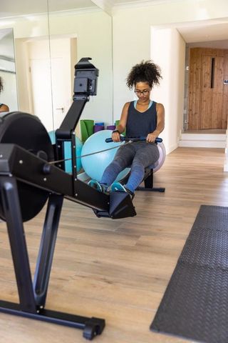 Woman exercising on rowing machine in home gym for fitness and wellness