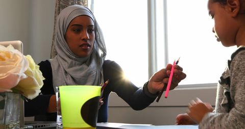 Young Mother in Hijab Teaching Daughter with Color Pencils at Home