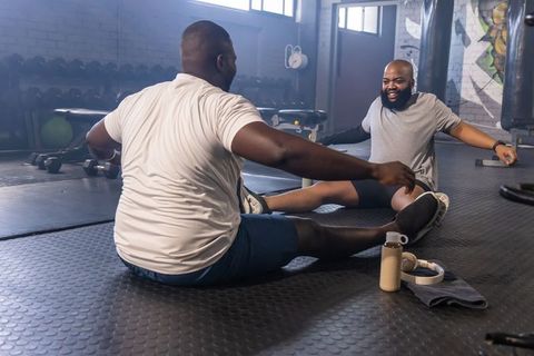 African men stretching together on gym floor building mobility and fitness partnership