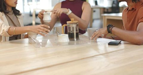 Diverse coworkers sharing coffee at wooden table in bright coworking space