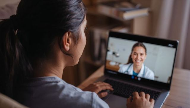 Young woman video consulting smiling doctor on laptop at home for telemedicine appointment