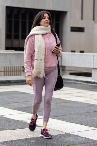 Urban woman walking in pastel activewear and long knit scarf holding phone and shoulder bag