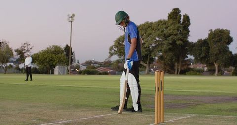 Teenage cricket batsman adjusting bat grip preparing to face bowler during evening match