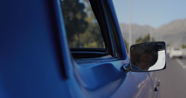 Close-up of a car's side mirror on a sunny day, with copy space. The mirror reflects the clear blue sky and hints of the road ahead.