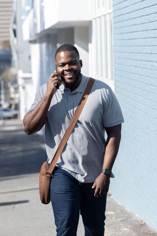 African-american man walking and talking on phone with crossbody bag and smartwatch