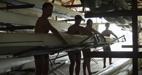 Team of Rowers Storing Boat in Boathouse During Sunny Day