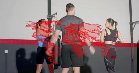 Fitness coach guiding trio through boxing drills hitting heavy bag with red motion smear