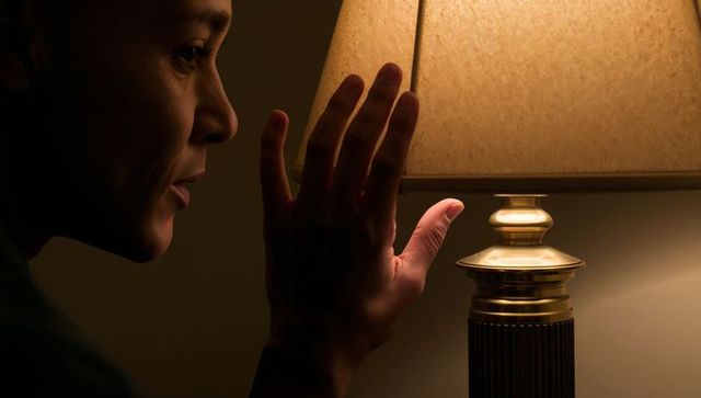 Woman reaching and adjusting bedside lamp warm glow closeup profile touching lampshade