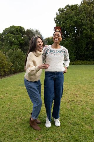 Laughing friends leaning on grass wearing cozy sweaters and denim, festive crowns