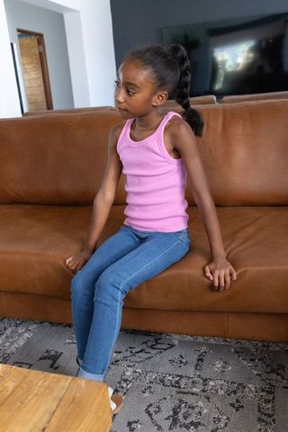 African american girl sitting on leather couch looking left wearing pink tank and jeans
