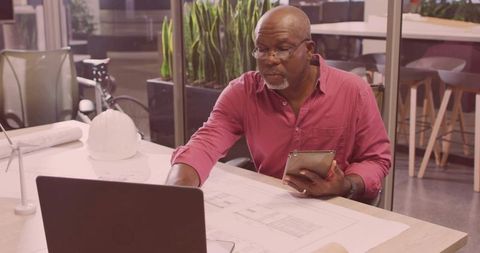 Architect reviewing blueprints on laptop tablet in modern office space