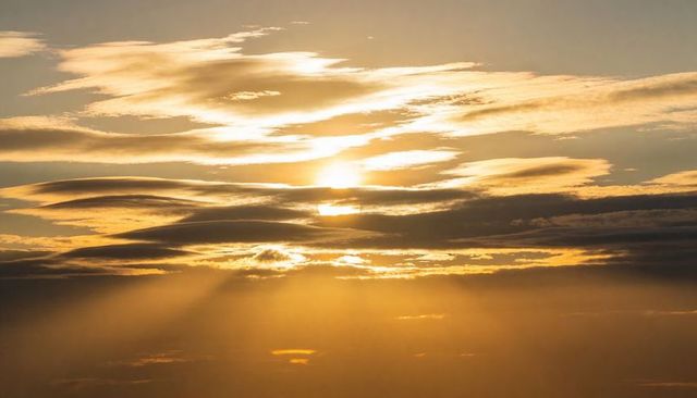 Golden crepuscular sunbeams piercing layered clouds over expansive horizon at golden hour