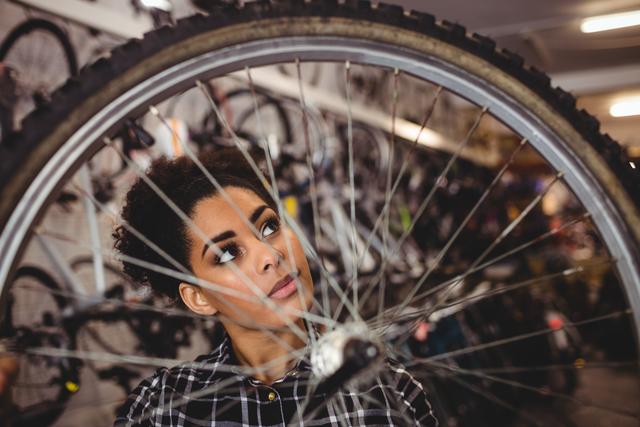 Woman bicycle mechanic attentively inspecting a bicycle wheel in a well-equipped workshop. Ideal for use in content related to bike repair services, maintenance tips, cycling enthusiasts, and gender diversity in technical professions.